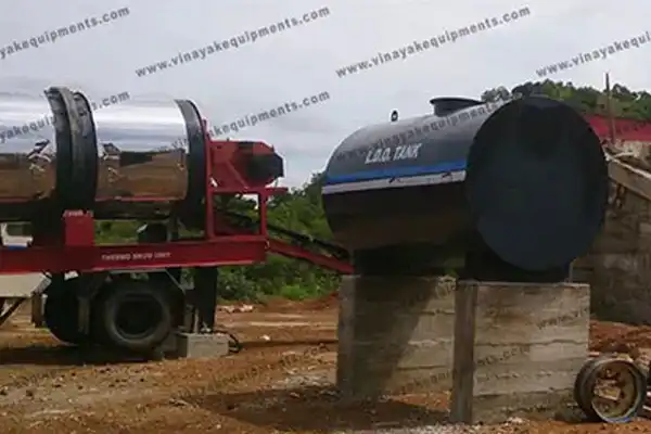 Industrial fuel/storage tanks on a red trailer and concrete blocks at a construction site. The polished stainless cylinder sits on a wheeled trailer beside a blue tank.